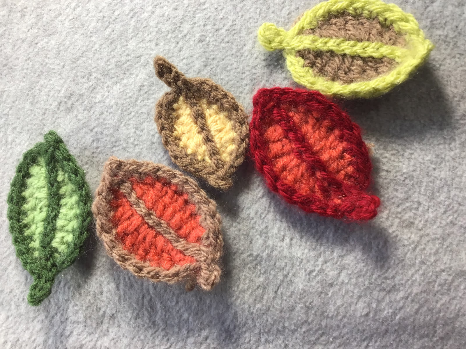 Five small crocheted leaves in autumn colors