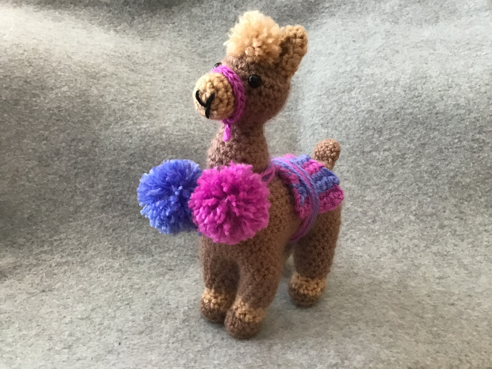 Crocheted llama with colorful pompoms and saddle