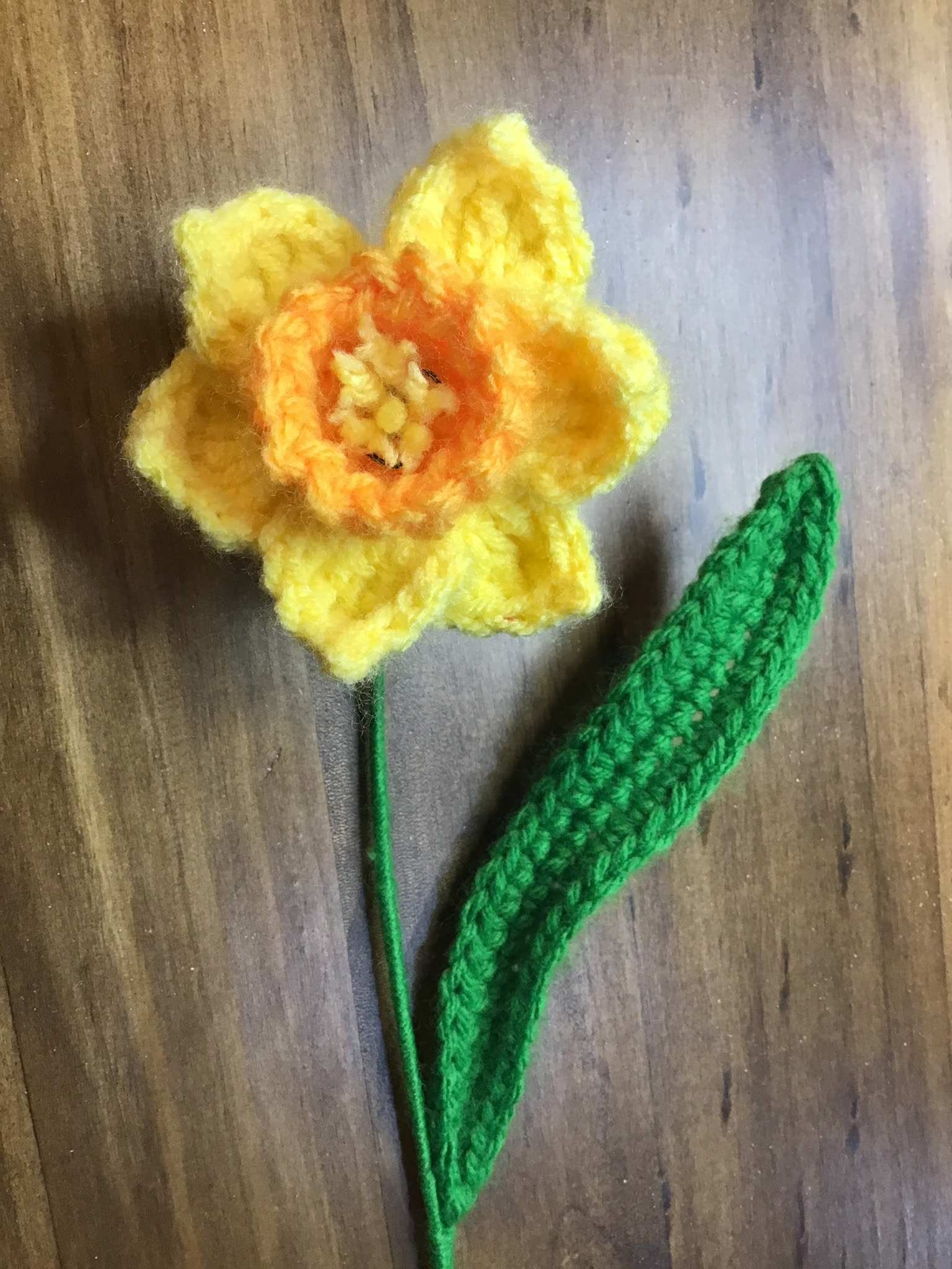 Yellow crocheted daffodil with green leaf