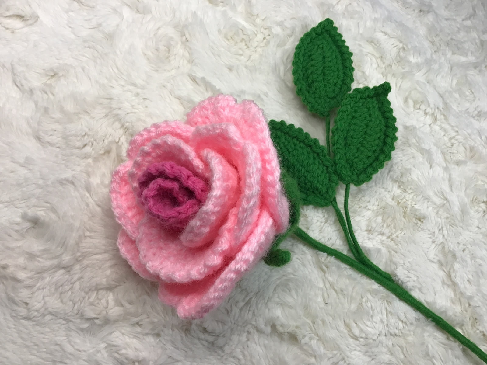 Large pink crocheted rose with three green leaves
