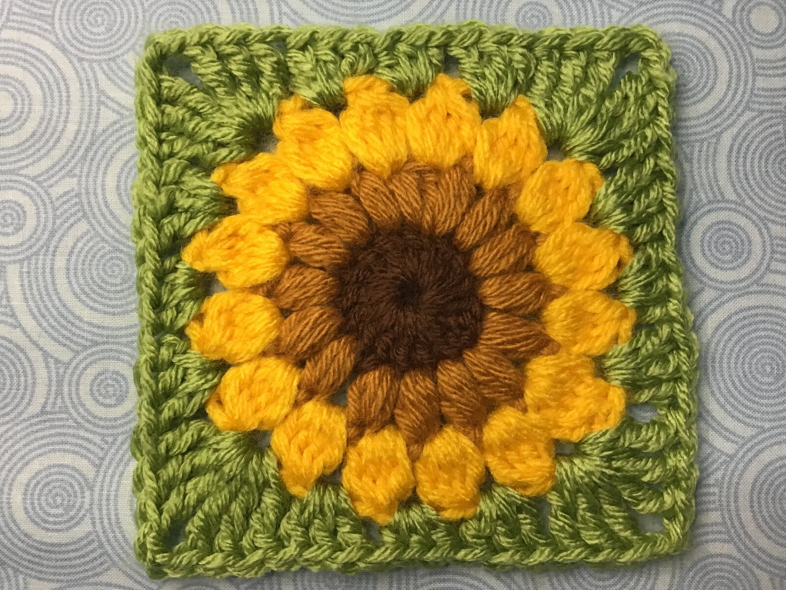 Crocheted sunflower granny square in yellow, brown, and green